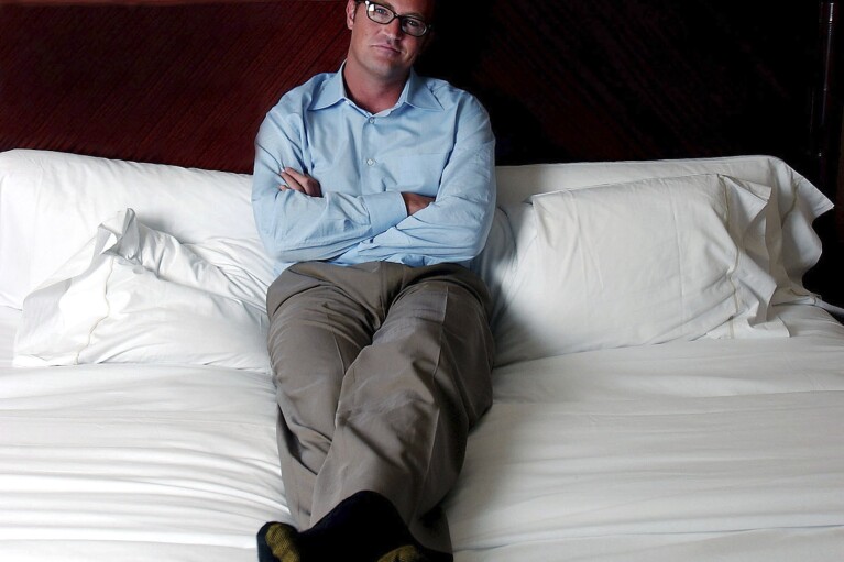 FILE - Actor Matthew Perry poses in his hotel bedroom in New York, Aug. 7, 2002. Perry, who starred as Chandler Bing in the hit series “Friends,” has died. He was 54. The Emmy-nominated actor was found dead of an apparent drowning at his Los Angeles home on Saturday, according to the Los Angeles Times and celebrity website TMZ, which was the first to report the news. Both outlets cited unnamed sources confirming Perry’s death. His publicists and other representatives did not immediately return messages seeking comment. (AP photo/Gino Domenico, File)