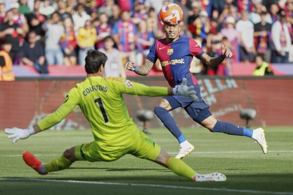 Barcelona's Raphinha shoots by Real Madrid's goalkeeper Thibaut Courtois during the La Liga soccer match between Barcelona and Real Madrid in Barcelona, Spain, Sunday, May 11, 2025. AP Photo/Joan Monfort)