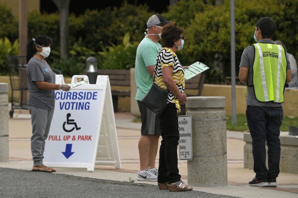 FILE - In this May 12, 2020 file photo, a voting official helps walk-up voters in a special election for California's 25th Congressional District during the coronavirus outbreak in Simi Valley, Calif. California's Democratic-controlled state Legislature is considering making it more difficult for local election officials to disqualify ballots. (AP Photo/Mark J. Terrill, File)