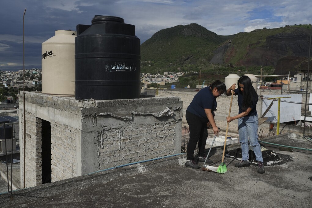 Sonia Estefania Palacios Diaz, left, and Lizbeth E. Pineda Castro, right, clean the roof of a house used to collect rainwater in the Iztapalpa neighborhood in Mexico City, Sunday, July 21, 2024. (AP Photo/ Marco Ugarte)