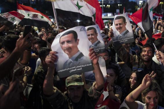 FILE - In this May 27, 2021 file photo, Syrian President Bashar Assad supporters hold up national flags and pictures of Assad as they celebrate at Omayyad Square, in Damascus, Syria. Jordan’s King Abdullah received a call from Syrian President Bashar Assad, Sunday, Oct. 3, 2021, the first between the two leaders after a decade of strained relations over Syria's civil war. (AP Photo/Hassan Ammar, File)