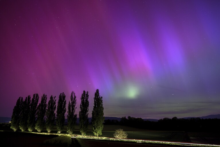 En esta fotografía de larga exposición, un automóvil pasa e ilumina los álamos mientras la aurora boreal brilla en el cielo nocturno sobre el pueblo de Daillens, Suiza, la madrugada del sábado 11 de mayo de 2024. (Laurent Gillieron/Keystone vía AP)