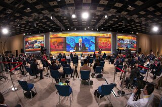 Russian President Vladimir Putin gestures as he speaks via video call during a news conference as journalists wearing face masks to protect against coronavirus, observe social distancing guidelines watch him at a big screen in Moscow, Russia, Thursday, Dec. 17, 2020. This year, Putin attended his annual news conference online due to the coronavirus pandemic. (AP Photo/Alexander Zemlianichenko)