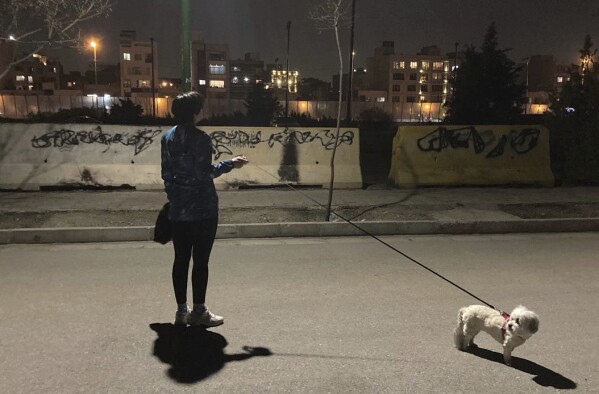 An Iranian woman without wearing her mandatory Islamic headscarf walks her dog at a park with graffiti against the government which is painted over in black, Monday, March 6, 2023. Iranians are marking the first anniversary of nationwide protests over the country's mandatory headscarf law that erupted after the death of a young woman detained by morality police. (AP Photo/Vahid Salemi)