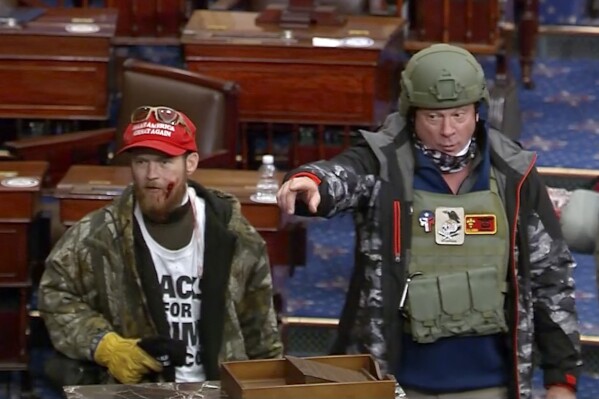 This image from Senate Television video, contained in the Justice Department's affidavit in support of a criminal complaint and arrest warrant for Larry Rendall Brock, shows Brock, right, on the floor of the Senate at the U.S. Capitol on Jan. 6, 2021, in Washington. A federal appeals court in Washington, on March 1, 2024, has ordered a new sentence for Brock, who stormed the U.S. Capitol dressed in combat gear, in a ruling that could impact dozens of other cases stemming from the Jan. 6, 2021, attack. While a panel of the U.S. Court of Appeals for the D.C. Circuit upheld Brock's conviction, the court said a judge wrongly applied an enhancement that lengthened the recommended prison sentence range under federal guidelines. (Department of Justice via AP)