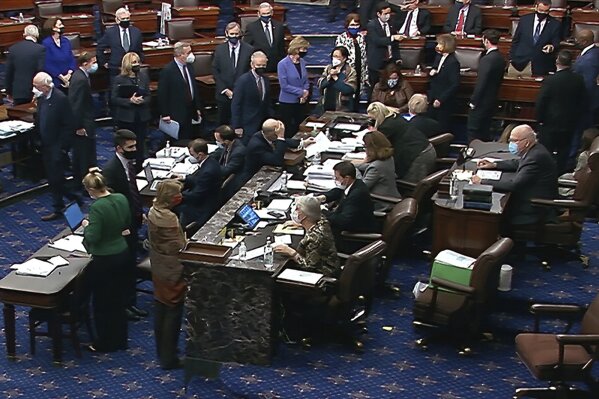In this image from video, Democratic senators stand as they wait for the announcement that the Senate version of the COVID-19 relief bill has passed by a vote of 50-49 in the Senate at the U.S. Capitol in Washington, Saturday, March 6, 2021. (Senate Television via AP)