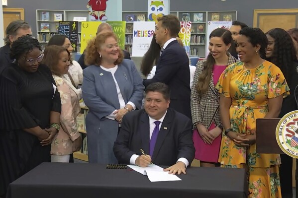 In this screenshot from a livestream broadcast by the State of Illinois, Gov. J.B. Pritzker signs a bill, Monday, June 12, 2023, at Harold Washington Library's Thomas Hughes Children's Library in downtown Chicago. The new law will require the state's libraries to uphold a pledge not to ban material because of partisan disapproval, starting on Jan. 1, 2024. If they refuse, they will not receive state funding. Pritzker said the law will make Illinois the first state in the nation to outlaw book bans. (State of Illinois via AP)