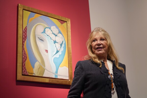 Pattie Boyd poses next to the original artwork by E. Frandsen De Schomberg, used for the cover of Derek and the Dominoes album 'Layla and Other Assorted Love Songs' as part of The Pattie Boyd Collection at Christie's, in London, Thursday, March 14, 2024. The artwork is estimated to sell £40,000-60,000. (AP Photo/Alberto Pezzali)