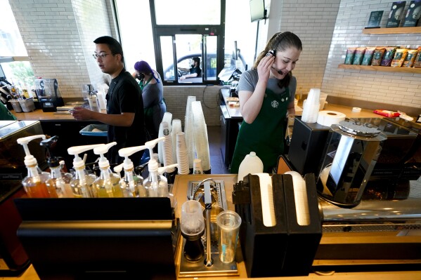 Harmony Mathison, right, uses a headset to talk to a customer at a Starbucks retail location, Wednesday, June 28, 2023, in Seattle. The company's goal is to cut waste, water use and carbon emissions in half by 2030. (AP Photo/Lindsey Wasson)