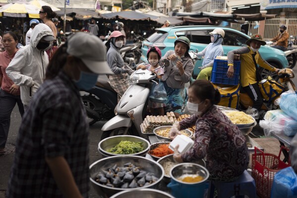 A shopper sitting on a scooter counts money after buying food from a street vendor in Ho Chi Minh City, Vietnam, Jan. 11, 2024. (AP Photo/Jae C. Hong)
