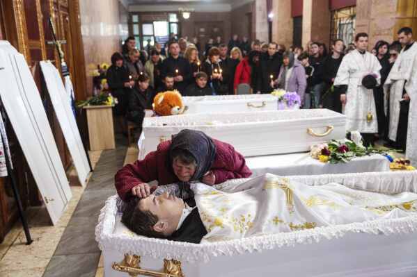 A grandmother says goodbye to her grandchildren Roman Martyniuk, 17, Tamara Martyniuk, 8, and Stanislav Martyniuk, 12, killed in a Russian strike on Sunday, during farewell ceremony in Korostyshiv, Zhytomyr region, Ukraine, Wednesday, May 28, 2025. (AP Photo/Evgeniy Maloletka)