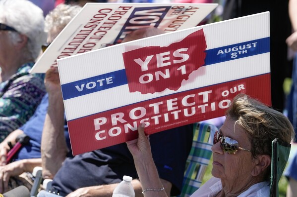 An attendee uses a sign to shield the sun during a "rosary rally" on Sunday, Aug. 6, 2023, in Norwood, Ohio. A national religious organization, Catholics for Catholics, gathered a lineup of anti-abortion influencers and conspiracy theorists from across the U.S. to speak at the rally to urge a “yes” vote on a ballot question in Ohio, known as Issue 1. If voters approve Issue 1, it would make it more difficult for an abortion rights amendment on the November ballot to succeed. (AP Photo/Darron Cummings)