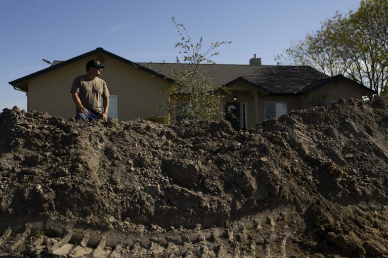 Earl Gomes, 33, stands for a photo outside his home with a berm he built to protect the property from possible flooding of the Kings River in the Island District of Lemoore, Calif., Thursday, April 20, 2023. After more than a dozen atmospheric rivers dumped record-setting rain and snowfall on California, residents find themselves facing the prospect of being trapped by rising rivers or flooded out. (AP Photo/Jae C. Hong)