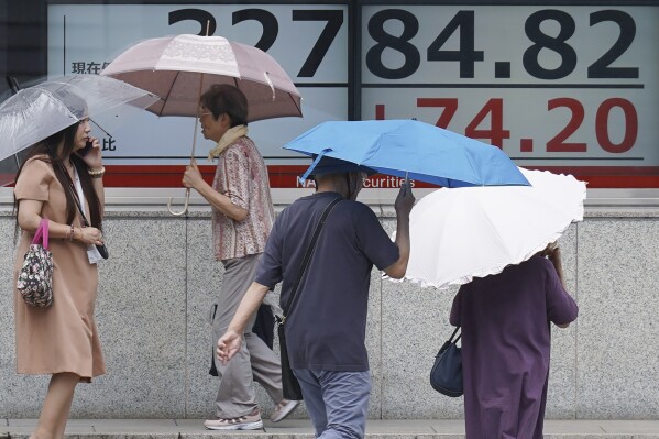 People walk in the rain in front of an electronic stock board showing Japan's Nikkei 225 index at a securities firm Monday, Sept. 4, 2023, in Tokyo. Stocks were higher in Asia on Monday after Wall Street was boosted by a report that signaled the US jobs market, while still healthy, is showing some signs of cooling. (AP Photo/Eugene Hoshiko)