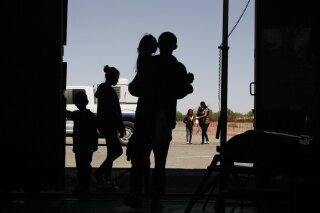 FILE - In this Wednesday, May 22, 2019 file photo migrants mainly from Central America guide their children through the entrance of a World War II-era bomber hanger in Deming, N.M. A panel of appeals court judges in California will hear arguments in the long-running battle between advocates for immigrant children and the U.S. government over conditions in detention and holding facilities near the southwest border. (AP Photo/Cedar Attanasio, File)