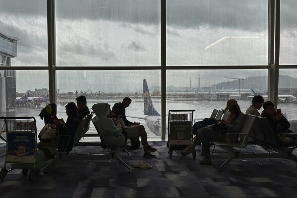 Travelers wait at the departures hall at Hong Kong International Airport in Hong Kong, Sunday, Oct. 8, 2023. Scores of flights in Hong Kong were canceled Sunday as Tropical Storm Koinu neared the southern Chinese city after leaving at least one dead and over 300 injured in Taiwan. (AP Photo/Emily Wang)