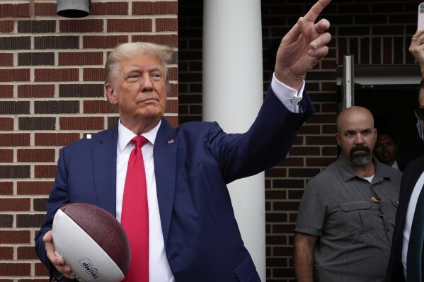 FILE - Former President Donald Trump holds a football before throwing it to the crowd during a visit to the Alpha Gamma Rho, agricultural fraternity, at Iowa State University before an NCAA college football game between Iowa State and Iowa, Sept. 9, 2023, in Ames, Iowa. Trump is set to attend South Carolina's biggest athletic event of the year, the Nov. 25 matchup between the University of South Carolina and Clemson University. (AP Photo/Charlie Neibergall, File)