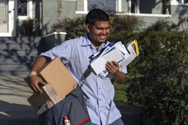 FILE - United States Postal Service letter carrier Gabriel Peña carries mail in Los Angeles on March 22, 2024. On Friday, June 7, 2024, the U.S. government issues its May jobs report. (AP Photo/Damian Dovarganes, File)