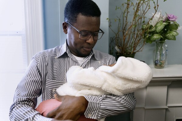 Ernseau Admettre holds his daughter Gabyana, Friday, Dec. 22, 2023, in a rectory building where they are staying at the Bethel AME Church in the Jamaica Plain neighborhood of Boston. Demand for shelter has increased as Massachusetts struggles to find newly arriving migrants places to stay after hitting a state-imposed limit of 7,500 families in its emergency homeless shelter system last month. (AP Photo/Michael Dwyer)