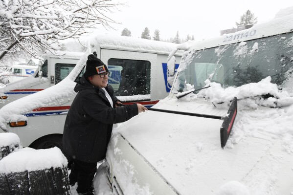 Mail carrier Kirsten Donner de-ices her delivery truck and prepares to make her deliveries on March 1, 2024, in Truckee, Calif.  The most powerful Pacific storm of the season is forecast to bring up to 10 feet of snow to the Sierra Nevada by the weekend (AP Photo/Andy Baron).