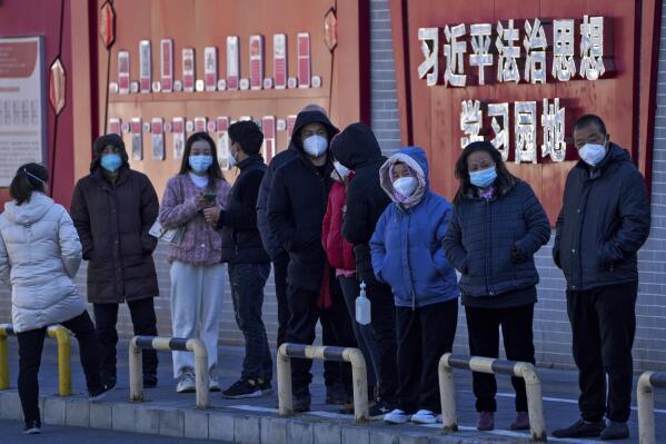 Residents wearing face masks line up for their routine COVID-19 tests along a wall displaying the words "Xi Jinping rule of law ideology learning ground" in Beijing, Monday, Dec. 5, 2022. China is easing some of the world's most stringent anti-virus controls and authorities say new variants are weaker. But they have yet to say when they might end a "zero-COVID" strategy that confines millions of people to their homes and set off protests and demands for President Xi Jinping to resign. (AP Photo/Andy Wong)