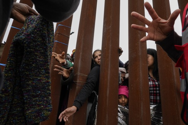 文件——2023年5月12日，圣地亚哥，移民穿过边境墙，领取志愿者分发的衣物，他们在两堵边境墙之间等待申请庇护。美国总统乔·拜登（Joe Biden）下令暂停美国与墨西哥边境的庇护程序，因非法入境而被逮捕的人数已超过每天2500人，并立即触发。（美联社照片/格雷戈里·布尔档案）