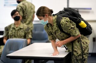 FILE - Inn this Aug. 24, 2020, file photo, a midshipman uses a sanitizing wipe to clean her desk before the start of a leadership class at the U.S. Naval Academy in Annapolis, Md. The U.S. Naval Academy is developing plans to begin vaccinating midshipmen in March 2021, so students can deploy out to ships and with Navy teams as part of their training this summer. (AP Photo/Julio Cortez, File)