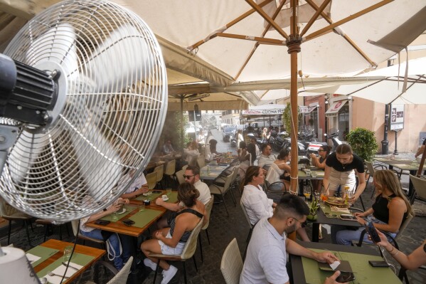 A fan sprays water to cool off customers at a restaurants in downtown Rome, Tuesday, July 25, 2023. Rising global temperatures are elevating air conditioning from a luxury to a necessity in many parts of Europe, which long has had a conflictual relationship with energy-sucking cooling systems deemed by many a U.S. indulgence. (AP Photo/Andrew Medichini)