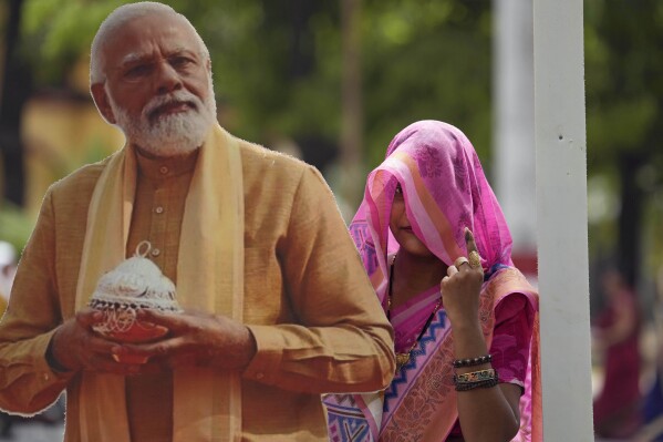 FILE-A woman shows her index fingers marked with an indelible ink as she poses for a photograph next to a cutout portrait of Indian Prime Minister Narendra Modi after casting her vote in the seventh and final phase of India's national elections, in Varanasi, India, Saturday, June 1, 2024. Indians began voting Saturday in the last round of a six-week-long national election that is a referendum on Hindu nationalist Prime Minister Narendra Modi's decade in power. (AP Photo/Rajesh Kumar Singh,file)