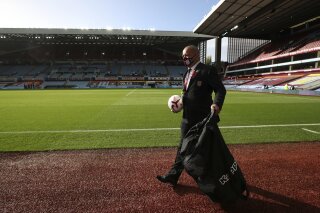 An Aston Villa member of staff wearing a mask holds a soccer ball as he walks by the pitch ahead of the English Premier League soccer match between Aston Villa and Southampton at Villa Park in Birmingham, England, Sunday, Nov. 1, 2020. The British Prime Minister Boris Johnson announced Saturday night that England will have further restrictive measures to combat the coronavirus pandemic starting Thursday, though the Premier league and other elite sport would continue. (Nick Potts via AP)