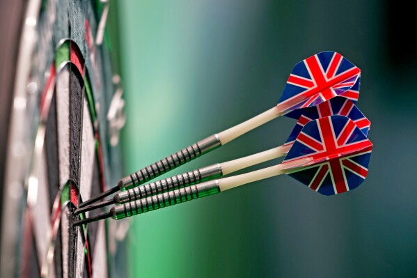 Three darts, with British union flag feathers, stick into the dart board as play continues in the quarterfinals of the World Darts Championship at Alexandra Palace in London, Monday, Jan. 1, 2024. (AP Photo/Kin Cheung)