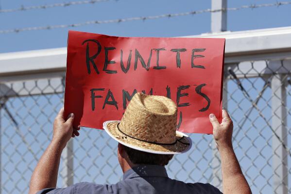 FILE - In this June 21, 2018 file photo, a protester holds a sign outside a closed gate at the Port of Entry facility in Fabens, Texas, where tent shelters were being used to house separated family members. The Biden administration is stepping up its effort to find and unite migrant families forcibly separated under President Donald Trump. (AP Photo/Matt York)