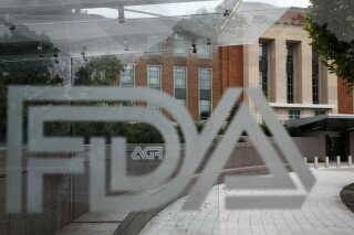 FILE - This Aug. 2, 2018, file photo shows the U.S. Food and Drug Administration building behind FDA logos at a bus stop on the agency's campus in Silver Spring, Md.  U.S. regulators have approved a new type of coronavirus test that administration officials have touted as a key to opening up the country. The Food and Drug Administration on Saturday, May 9, 2020, announced emergency authorization for antigen tests developed by Quidel Corp. of San Diego. The test can rapidly detect fragments of virus proteins in samples collected from swabs inside the nasal cavity, the FDA said in a statement. (AP Photo/Jacquelyn Martin, File)