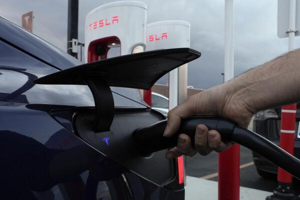 FILE - A motorist charges his electric vehicle at a Tesla Supercharger station in Detroit, Wednesday, Nov. 16, 2022. About half of U.S. adults say they are not likely to go electric when it comes time to buy a new vehicle, a new poll by The Associated Press-NORC Center for Public Affairs Research and the Energy Policy Institute at the University of Chicago shows. (AP Photo/Paul Sancya, File)