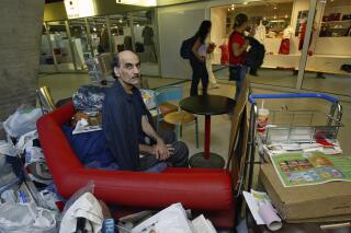 FILE - Merhan Karimi Nasseri sits among his belongings at Terminal 1 of Roissy Charles De Gaulle Airport, north of Paris on Aug. 11, 2004 . An Iranian man who lived for 18 years in Paris' Charles de Gaulle Airport and inspired the Steven Spielberg film "The Terminal" died Saturday, Nov. 12, 2022 in the airport, officials said. Merhan Karimi Nasseri died after a heart attack in the airport's terminal 2F around midday, according an official with the Paris airport authority. Police and then a medical team treated him but were not able to save him, the official said. (AP Photo/Michel Euler, File)