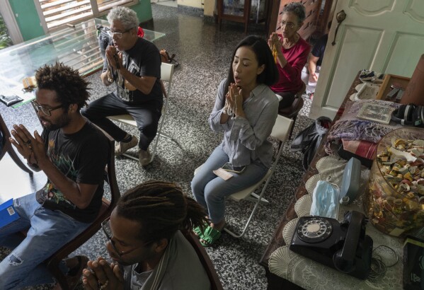 Twin brothers Yasnel and Yasmel Quintana, bottom left, meditate in the home of Cuban jazz musician Cesar Lopez, back left, and his wife Seiko Ishii, right center, in Havana, Cuba, Sunday, Feb. 4, 2024. Ten years ago, the Quintana twins who were raised in an Afro-Cuban family that follows Santeria, joined the local branch of the Soka Gakkai, a global Japanese Buddhist organization. (AP Photo/Ramon Espinosa)