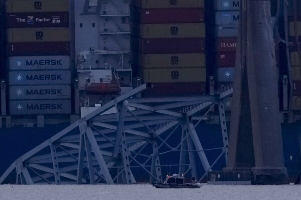 A container ship rests against wreckage of the Francis Scott Key Bridge as night falls on Tuesday, March 26, 2024, as seen from Sparrows Point, Md. The ship rammed into the major bridge in Baltimore early Tuesday, causing it to collapse in a matter of seconds and creating a terrifying scene as several vehicles plunged into the chilly river below. (AP Photo/Matt Rourke)