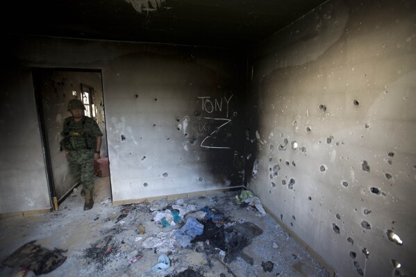 A soldier enters a bullet-riddled home covered by the initials of the Gulf Cartel (CDG) and Zetas (Z) in Ciudad Victoria, Tamaulipas state, Mexico, Sept. 6, 2014. (AP Photo/Eduardo Verdugo, File)
