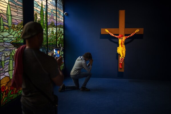 A visitor poses for a photo next to a Jani Leinonen artwork called Mc Jesus, at Barcelona's Museum of Forbidden Art in Barcelona, Spain, Friday, Nov. 17, 2023. In 2019, the Christian community in Haifa demanded de removal of Leinonen artwork from the city's museum, considering it offensive. A new museum in Barcelona is offering a second chance to controversial artworks that have suffered censorship for religious, sexual, political or commercial reasons. (AP Photo/Emilio Morenatti)