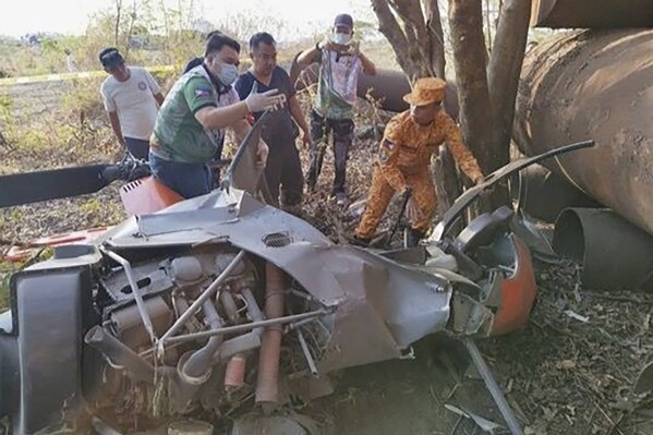 In this photo provided by the Cavite Police Regional PIO, rescuers check the remains of a trainer helicopter after it crashed in Cavite province, Philippines on Thursday April 11, 2024. The Philippine navy training helicopter crashed Thursday in a grassy area near a city public market south of the capital, the military and police said. (Cavite Police Regional PIO 4A via AP)