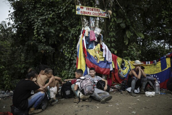 FILE - Migrants sit under a sign marking the Panama-Colombia border during their trek across the Darien Gap, May 9, 2023. Overwhelmed by the resurgence of migrants crossing the Darien jungle on the border with Colombia, the government of Panama announced on Thursday, Aug. 24, 2023, that it will take concrete measures. (AP Photo/Ivan Valencia, File)