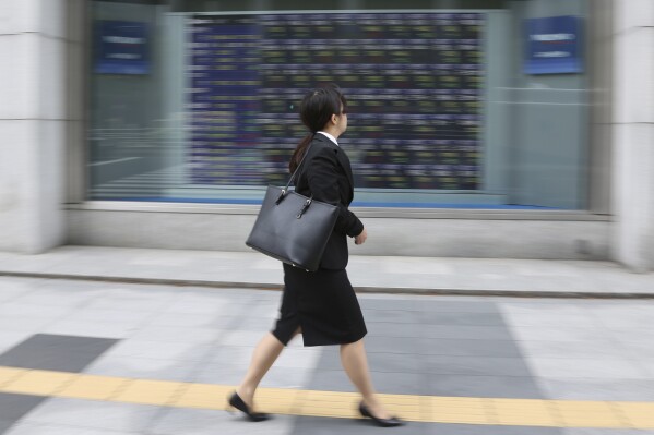 FILE - A woman walks by an electronic stock board of a securities firm in Tokyo, Tuesday, April 17, 2018. A powerful Japanese business lobby Keidanren has called on the government to quickly revise its civil law to allow married couples an option to keep separate surnames, because the current one-surname-per-household requirement causing most women to adopt their partners’ names has become a growing obstacle and even a business risk. (AP Photo/Koji Sasahara, File)