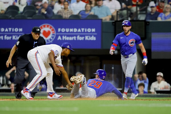 Chicago Cubs' Michael Busch (29) scores on a wild pitch as Texas Rangers pitcher José Leclerc, left, attempts the tag during the ninth inning of a baseball game Thursday, March 28, 2024 in Arlington, Texas. (AP Photo/Gareth Patterson)