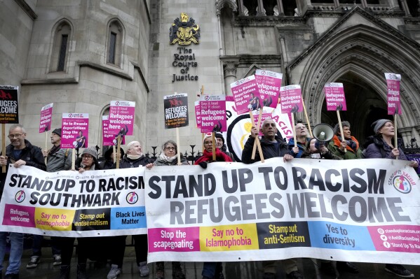 Stand Up To Racism campaigners hold banners outside the High Court in London, Monday, Dec. 19, 2022. (AP Photo/Kirsty Wigglesworth, File)