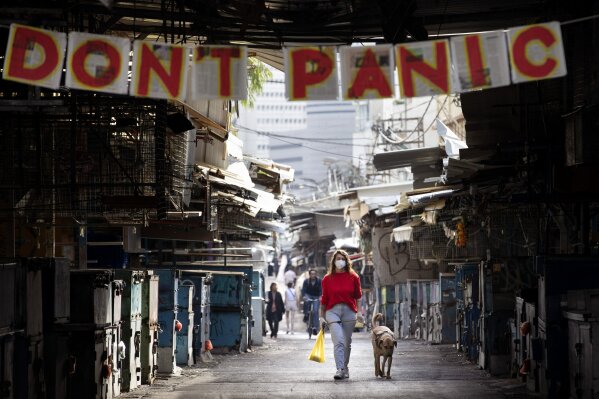 A woman walks her dog under a "don't panic" sign hanging on the entrance of a food market that was shut down in order to reduce the spread of the coronavirus, in Tel Aviv, Israel, Monday, March 23, 2020. In Israel daily life has largely shut down with COVID-19 cases multiplying greatly over the past week. (AP Photo/Oded Balilty)