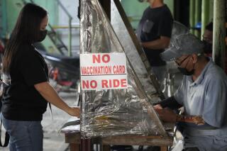 A woman stands beside a sign to remind passengers to show their vaccination card before riding at a jeepney terminal in Quezon city, Philippines on Monday, Jan. 17, 2022. People who are not fully vaccinated against COVID-19 were banned from riding public transport in the Philippine capital region Monday in a desperate move that has sparked protests from labor and human rights groups. (AP Photo/Aaron Favila)