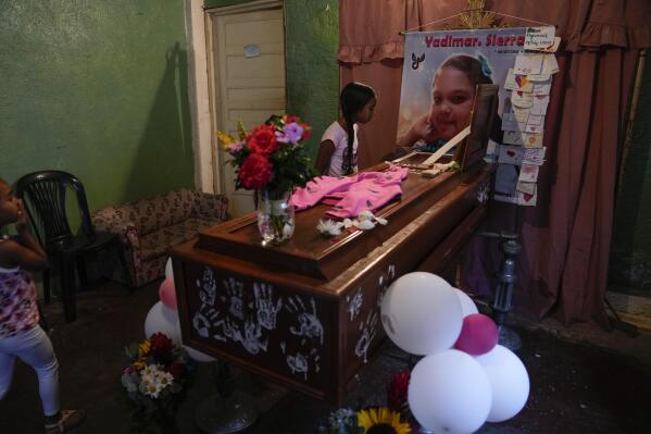 A girl looks into the open casket of Yadimar Sierra, 11, during her wake inside her home in the Petare neighborhood of Caracas, Venezuela, Sunday, Nov. 20, 2022. A week earlier, Yadimar was fatally hit by a stray bullet while she was sleeping in her home, according to her family. (AP Photo/Ariana Cubillos)