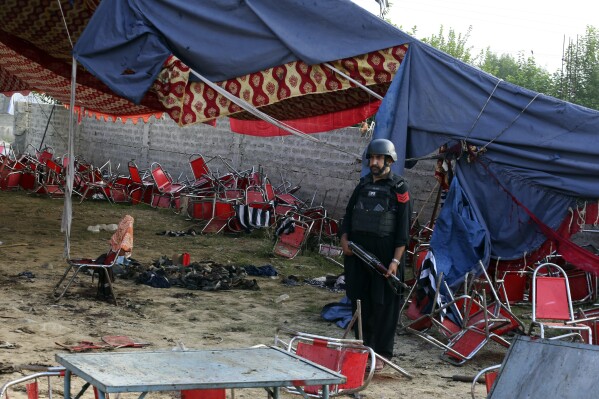 A Pakistani police officer stands guard at the aftermath of Sunday's suicide bomber attack in the Bajur district of Khyber Pakhtunkhwa, Pakistan, Monday, July 31, 2023. A suicide bomber blew himself up at a political rally in a former stronghold of militants in northwest Pakistan bordering Afghanistan on Sunday, killing and wounding multiple people in an attack that a senior leader said was meant to weaken Pakistani Islamists. (AP Photo/Mohammad Sajjad)