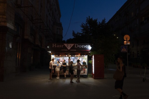 FILE - People wait for their food at a kiosk as dusk settles over Kyiv, Ukraine, Monday, July 3, 2023. (AP Photo/Jae C. Hong, File)
