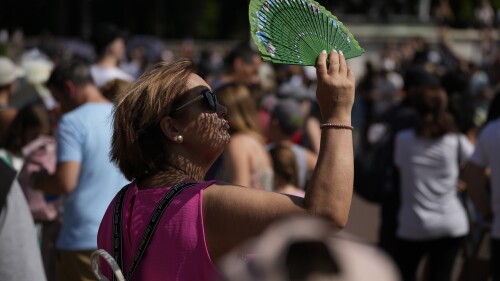 FILE - A tourist uses a fan to shade her face from the sun while waiting to watch the Changing of the Guard ceremony outside Buckingham Palace, during hot weather in London, July 18, 2022. Crushing temperatures that blanketed Europe during the summer of 2022 may have led to more than 61,000 heat-related deaths, according to a study published Monday, July 10, 2023. (AP Photo/Matt Dunham, File)